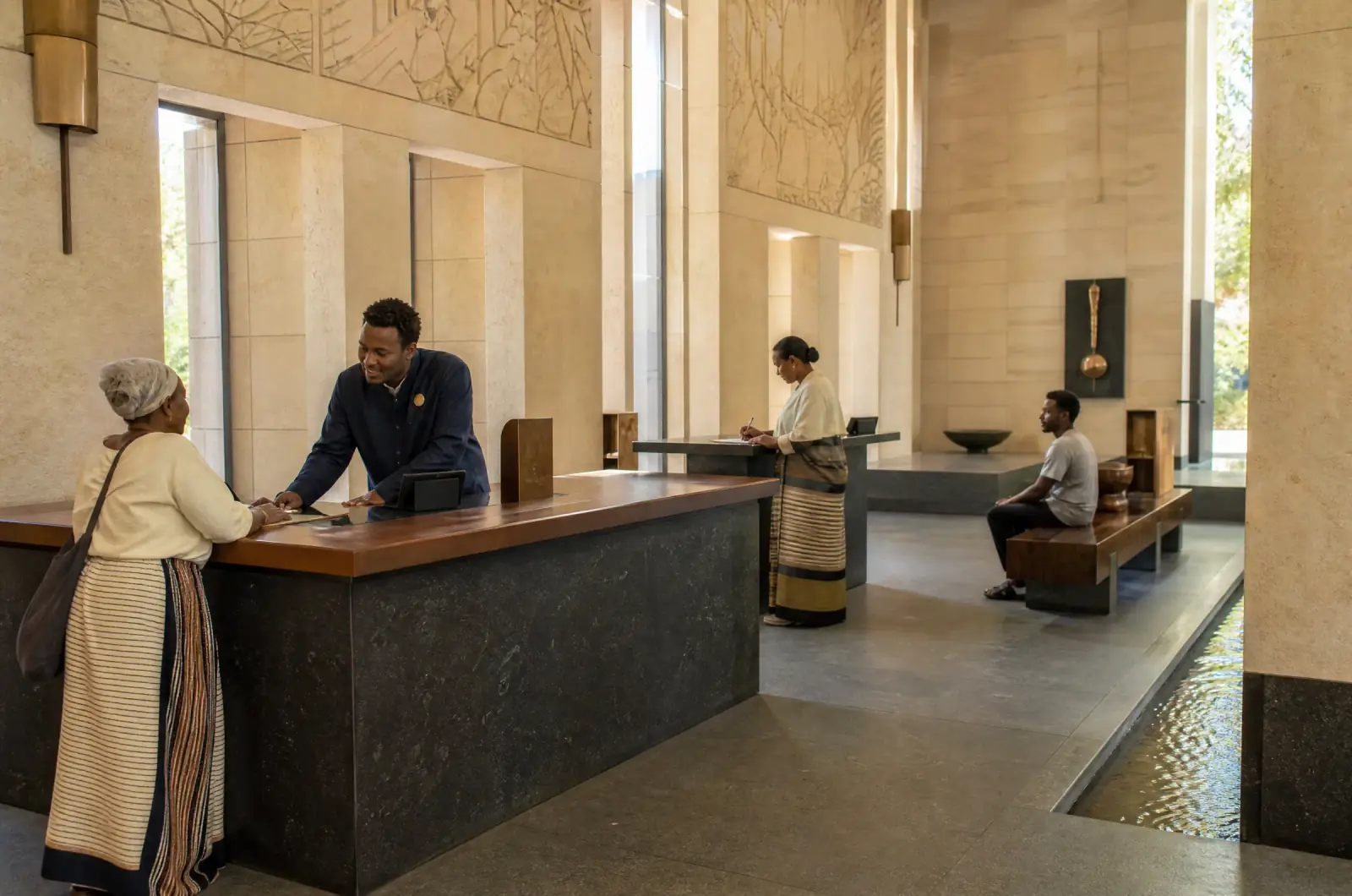 The public hall of the Office of the Crown: a civil servant helps an elderly woman at a counter of basalt and dark wood, daylight from high openings.